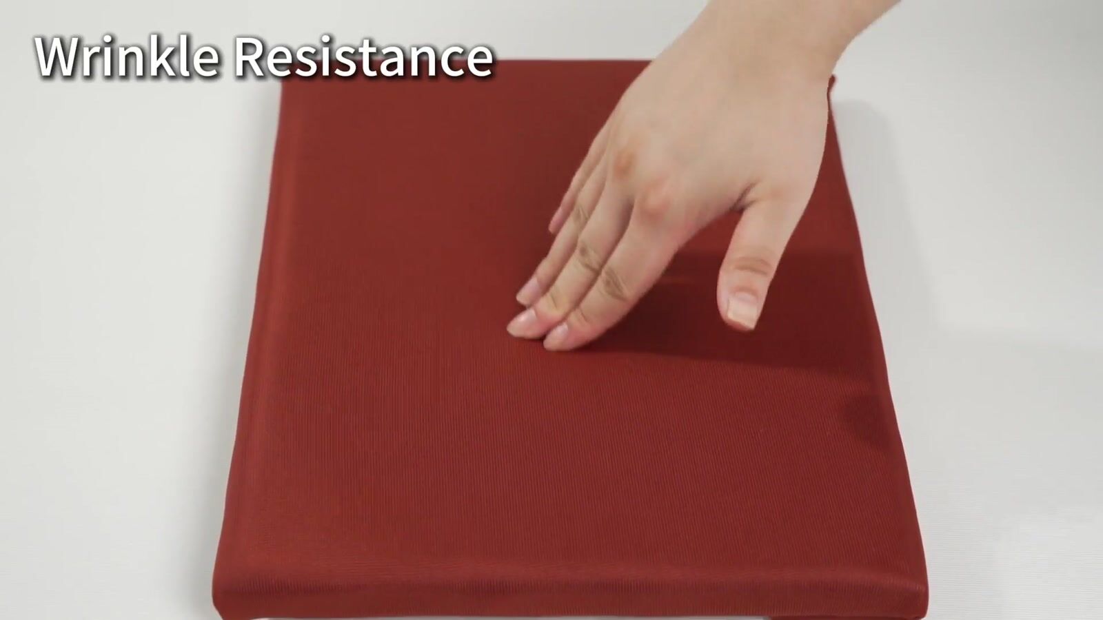 A hand pressing a red fabric-covered sample to demonstrate surface recovery