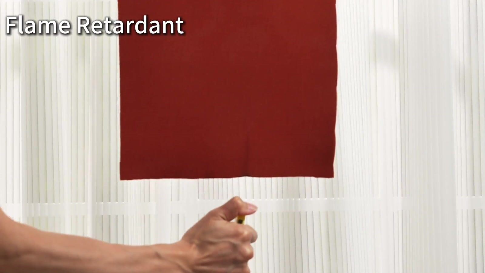 A flame being applied to the lower edge of a red fabric sample in a small-scale demonstration